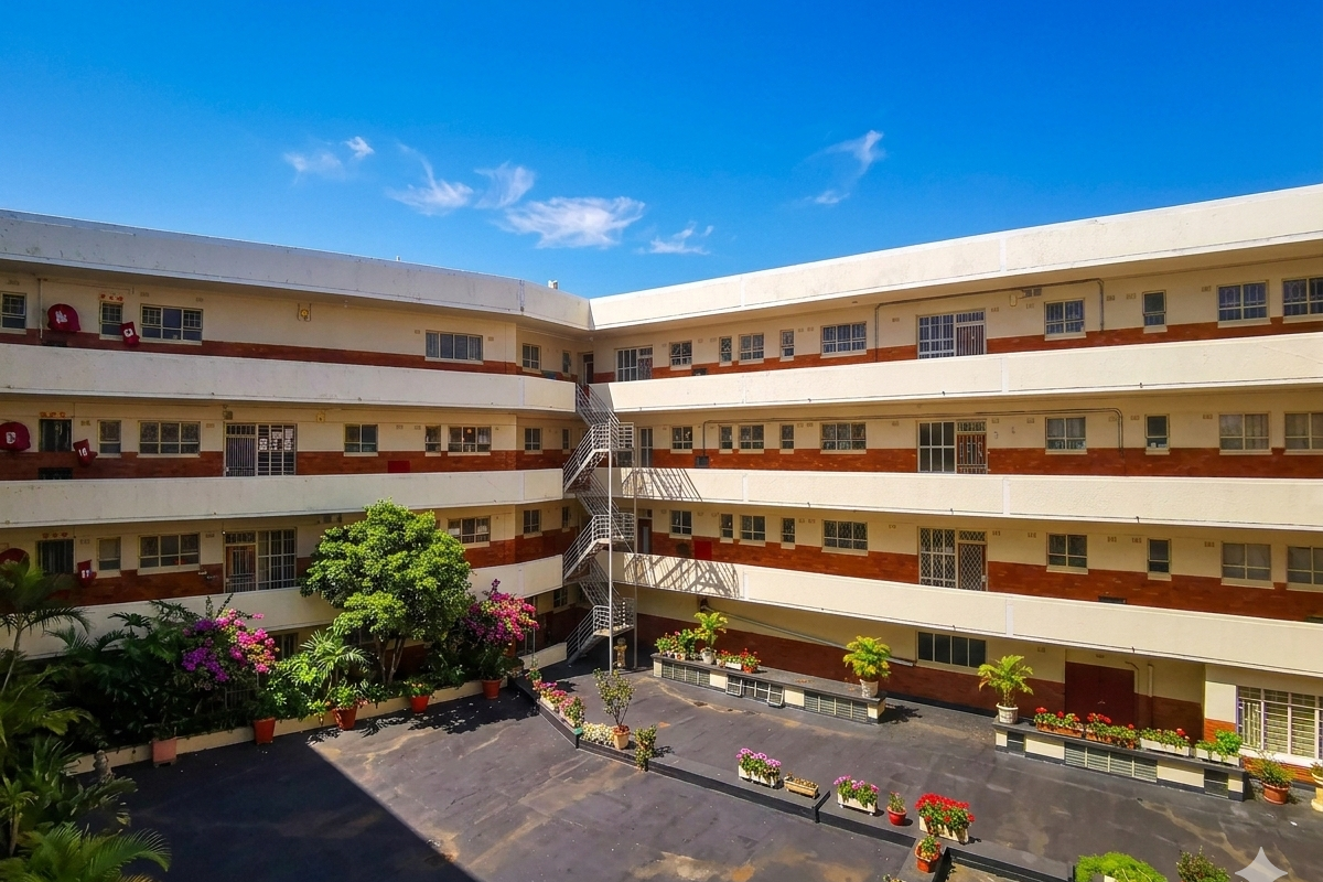 An elevated view of an apartment complex courtyard featuring multi-story brick and plaster facades, external staircases, and a paved central area with landscaped planters.
