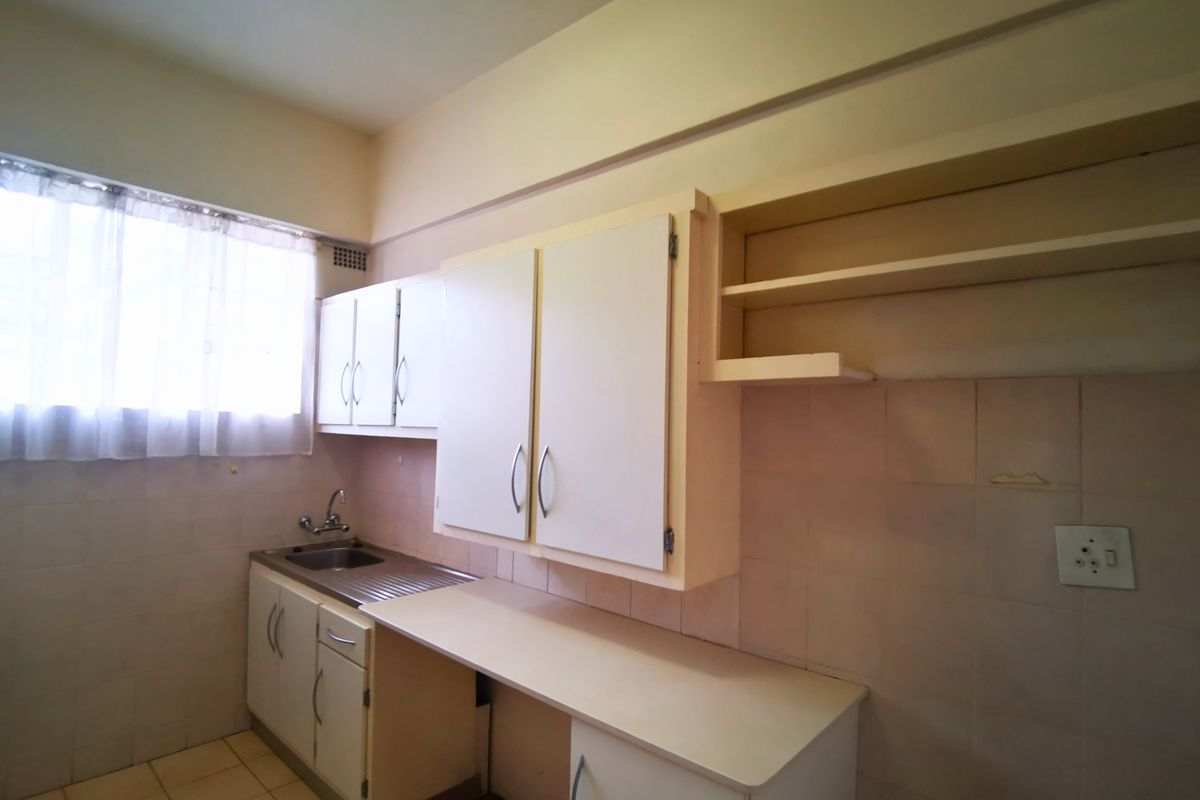 A dated kitchen featuring original cabinetry, a stainless steel sink, and tiled walls, offering a blank canvas for a modern renovation.