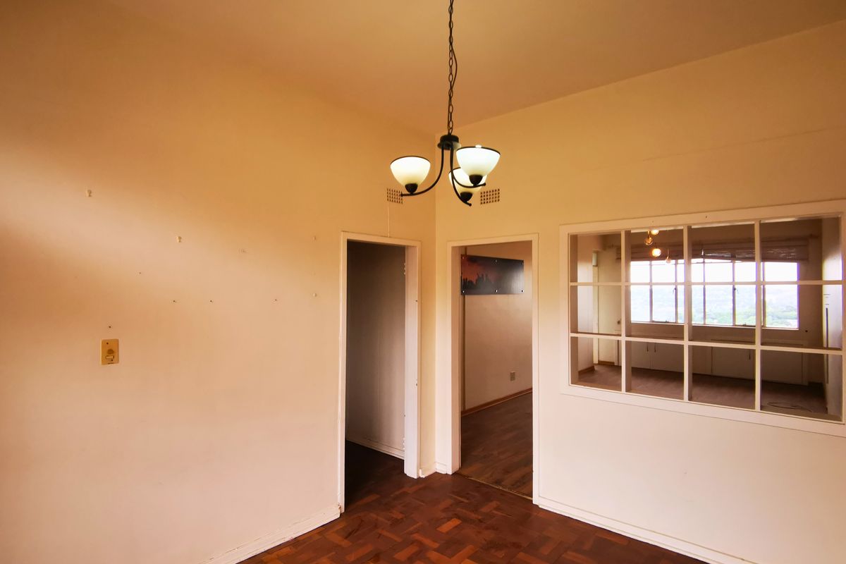 An empty living area featuring original parquet flooring, a central pendant light, and an internal window partition looking into an adjacent room.