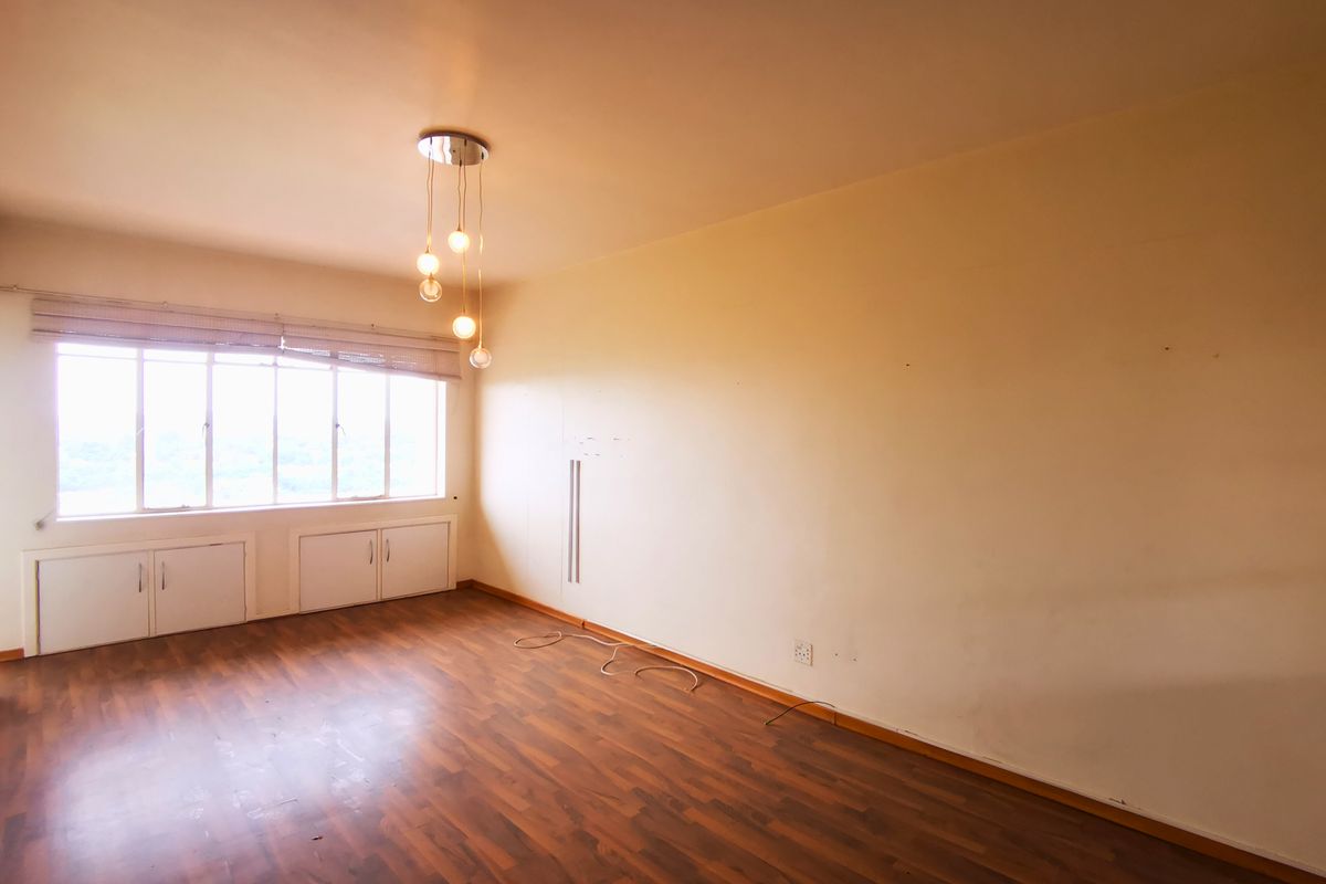 A spacious, empty bedroom featuring wood-look flooring, built-in under-window cabinetry, and a modern pendant light fixture.