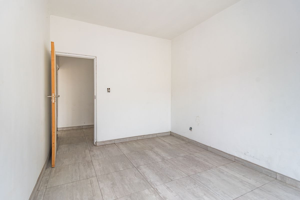 An empty, neutral-toned room featuring tiled flooring and a doorway leading to an adjacent space, ready for customization.
