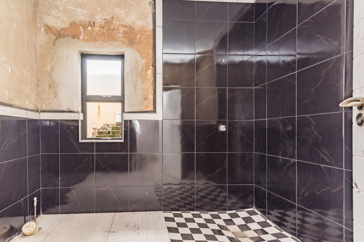 A bathroom in the process of renovation, featuring dark wall tiles, a checkered floor, and unfinished plasterwork around the window.