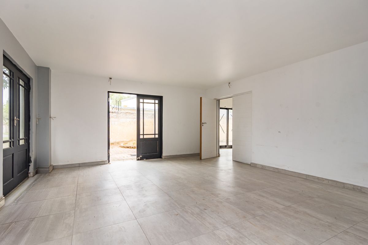 An empty, neutral living space featuring large tiled flooring, multiple access points to the exterior, and clean white walls ready for personalization.