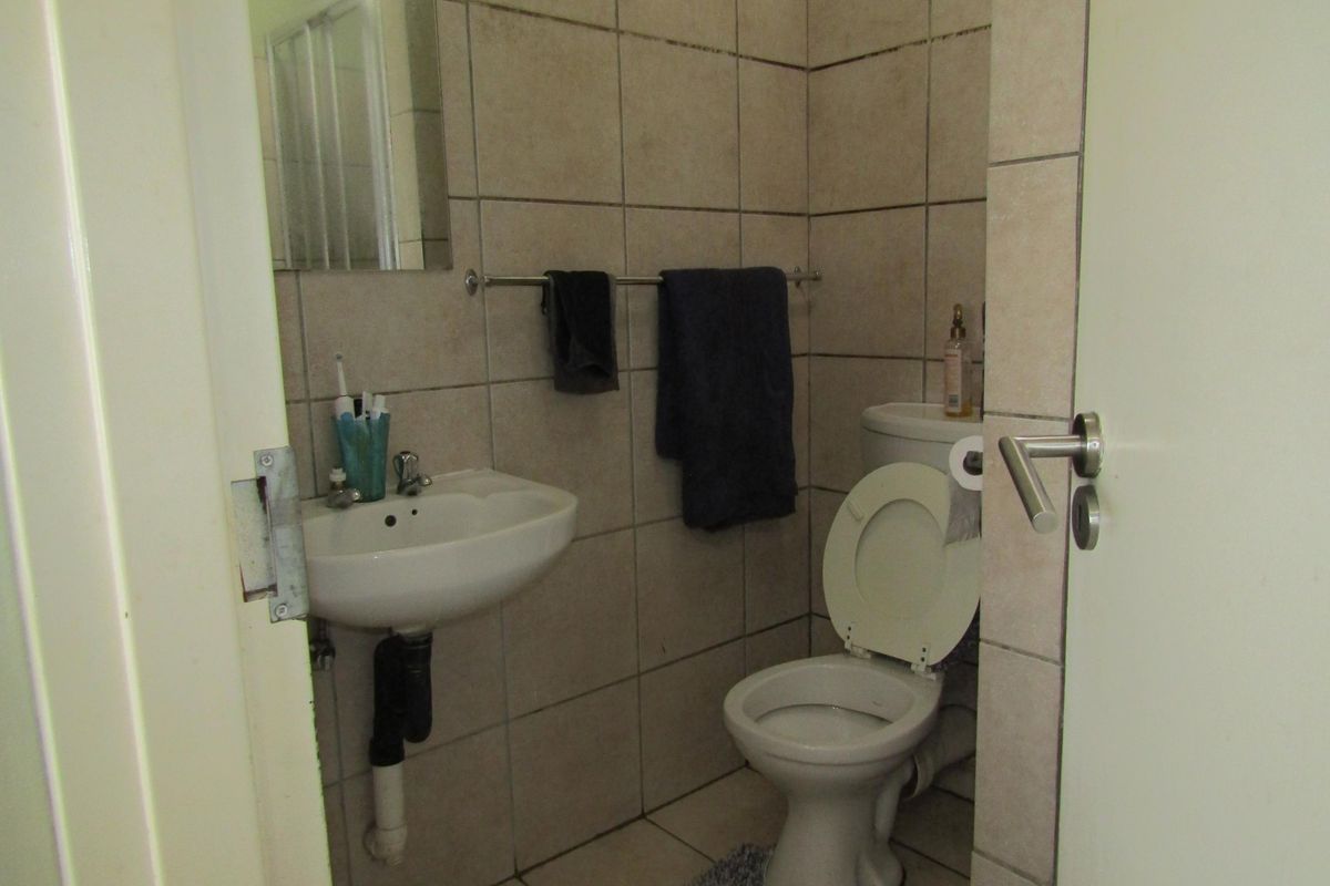 A compact bathroom featuring tiled walls and flooring, a wall-mounted basin, and a standard toilet suite.