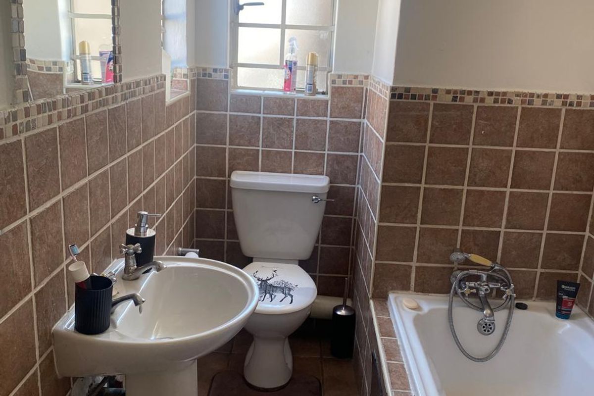 A compact bathroom featuring a pedestal basin, toilet, and bathtub with brown tiled walls and flooring, requiring minor repairs to the basin area.