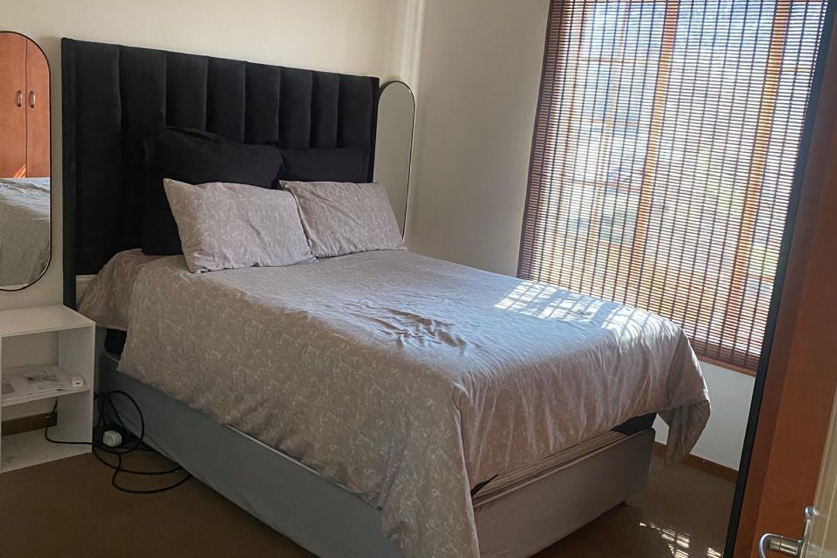 A functional bedroom featuring carpeted flooring, a ceiling light fixture, and bamboo window blinds providing natural light control.
