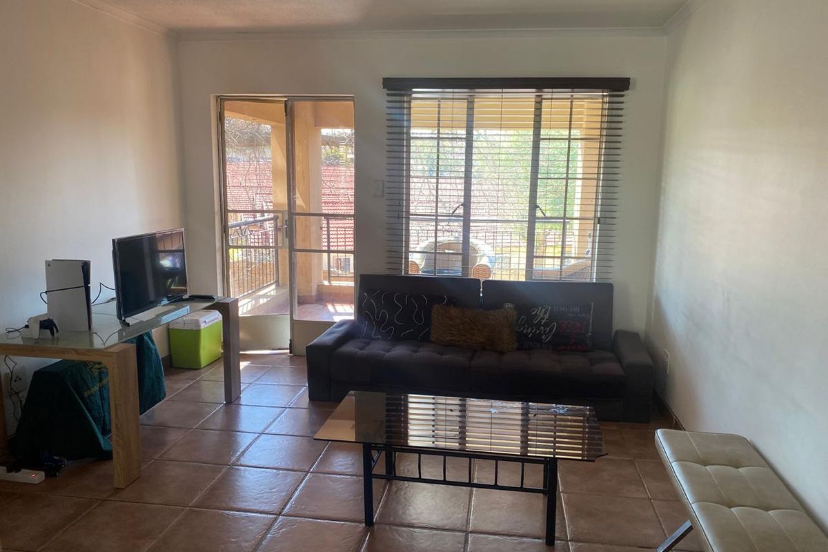 A living room featuring tiled flooring, a sliding glass door leading to a balcony, and large windows with venetian blinds.