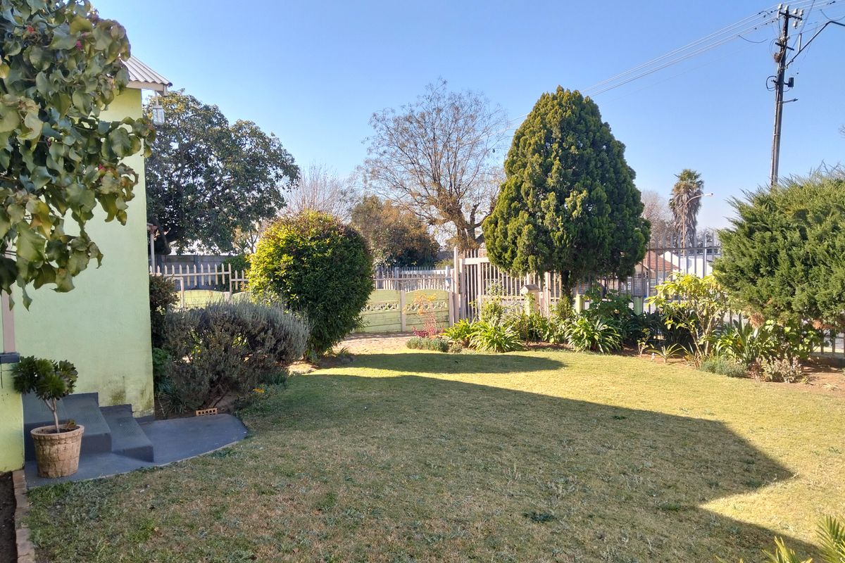 A well-maintained rear garden featuring a lawn, established trees, and secure perimeter fencing with a metal gate.