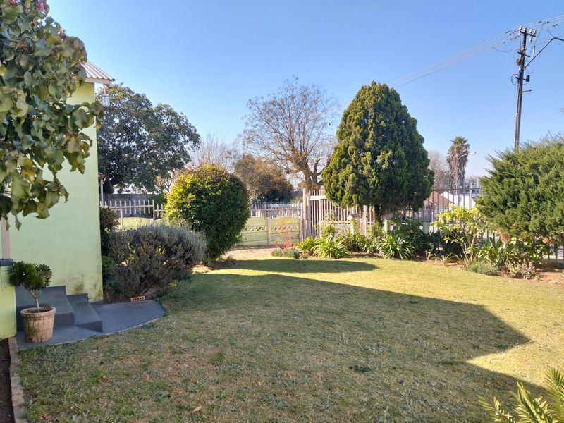 A well-maintained rear garden featuring a lawn, established trees, and secure perimeter fencing with a metal gate.