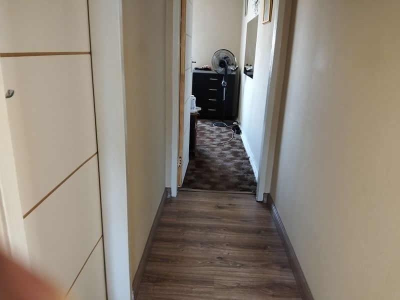 A narrow hallway featuring laminate flooring and a built-in cupboard, leading into an adjacent room.