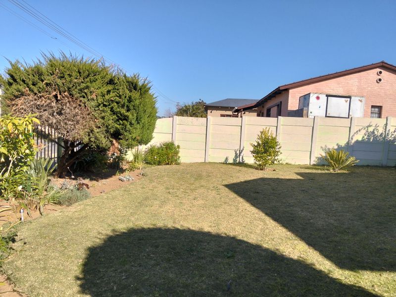 A private rear garden featuring a lawn area, established shrubbery, and a precast concrete boundary wall.