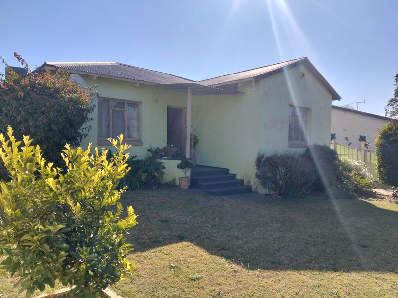 Front elevation of a single-story house featuring a corrugated metal roof, concrete entrance steps, and established garden area.