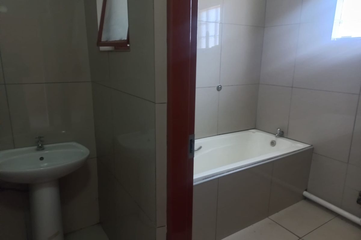 A functional bathroom featuring a pedestal basin and a built-in bathtub with full-height wall tiling.