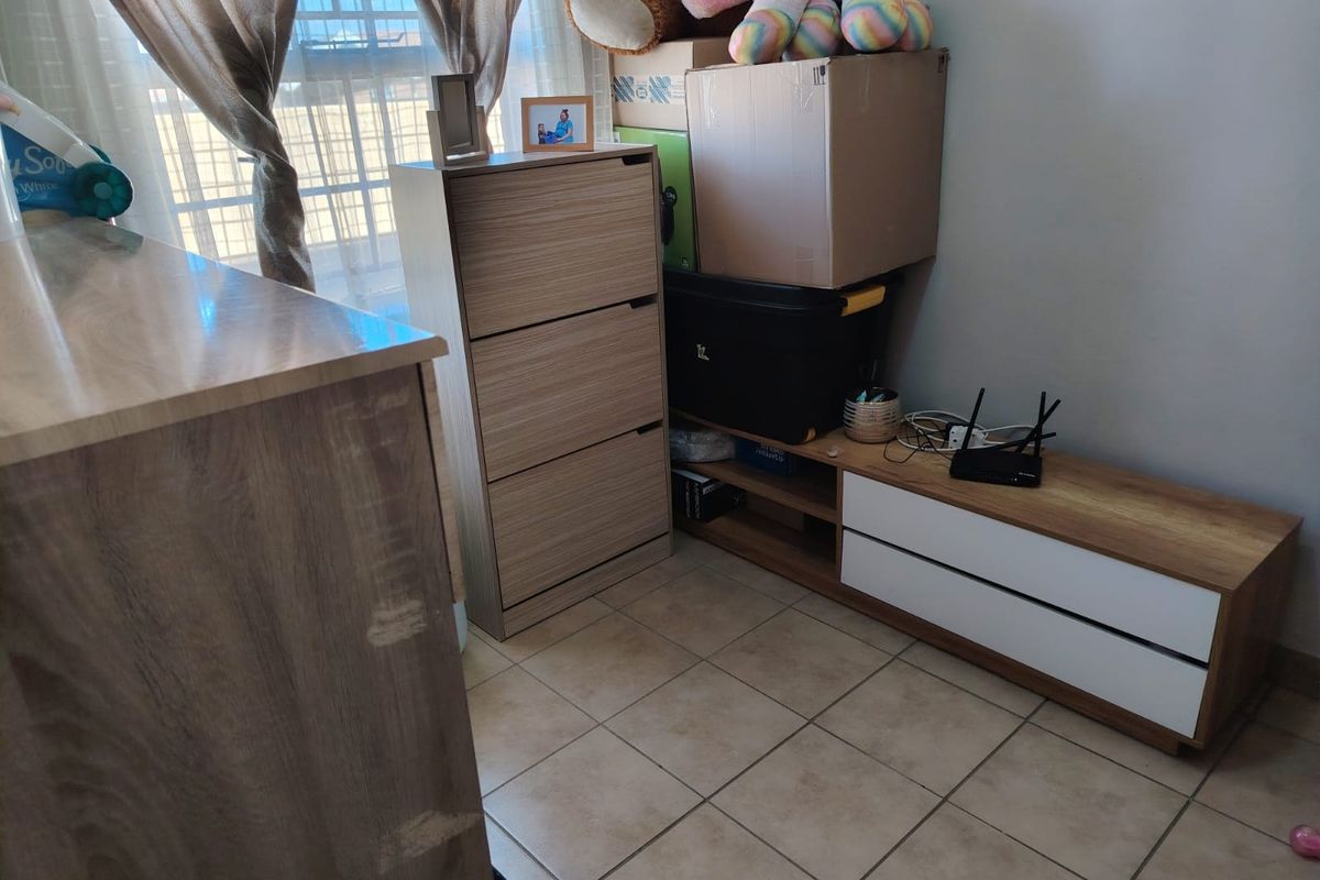 A bedroom interior featuring tiled flooring and a window with curtains, currently used for storage.