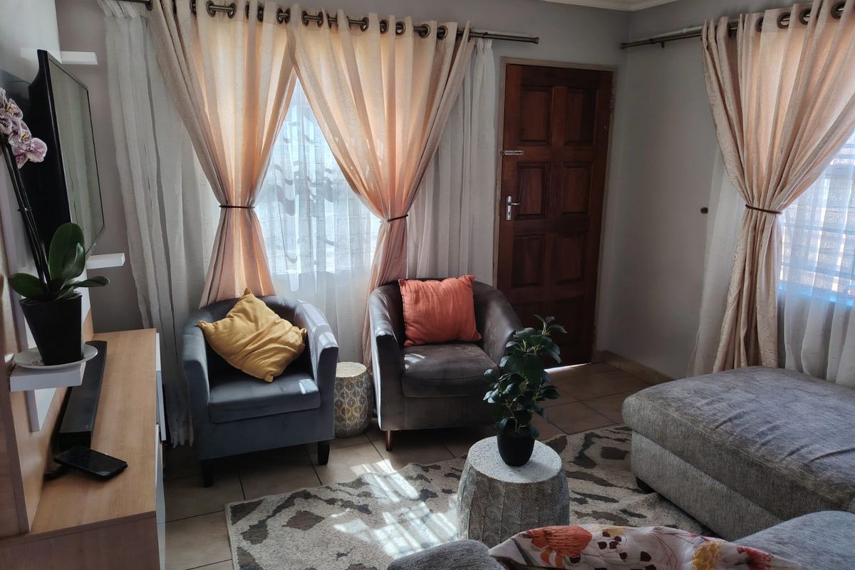 A cozy living room featuring tiled flooring, a solid timber door, and large windows with curtain treatments, providing a comfortable and functional living space.