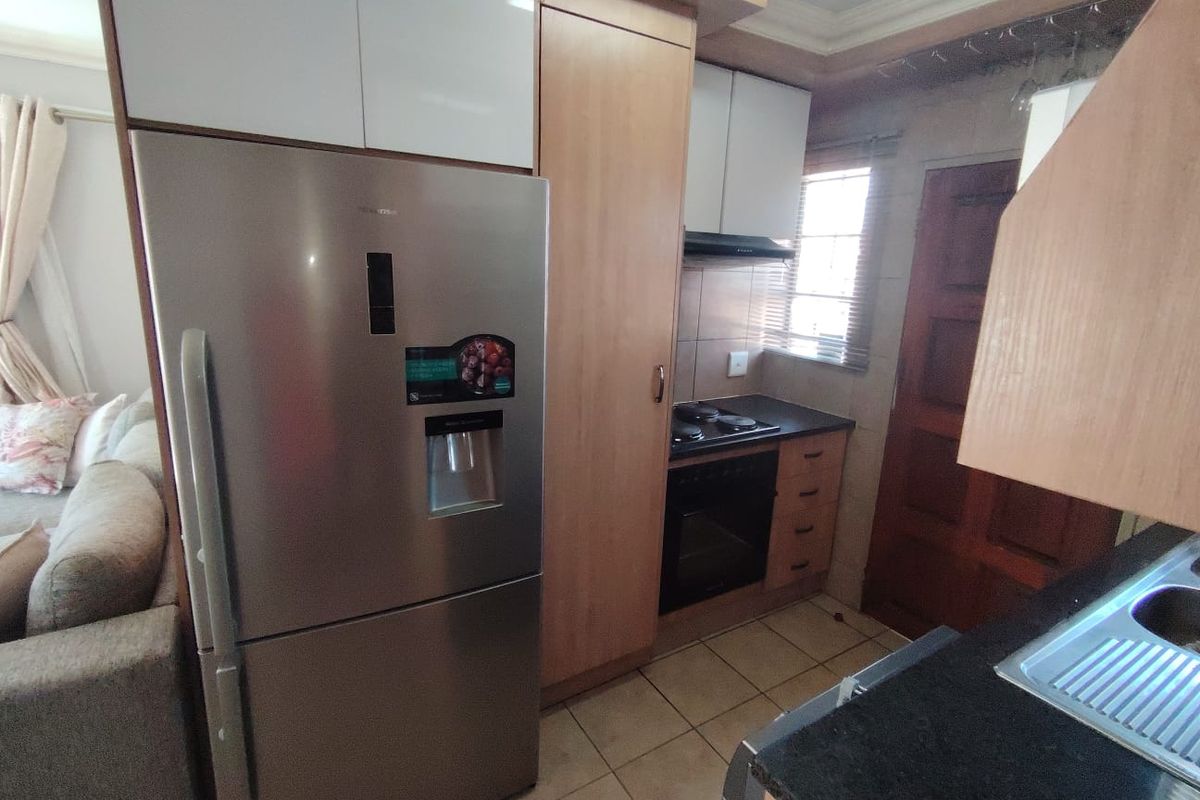 Compact kitchen featuring built-in cabinetry, integrated oven and hob, tiled flooring, and a stainless steel sink, seamlessly connected to the living area.