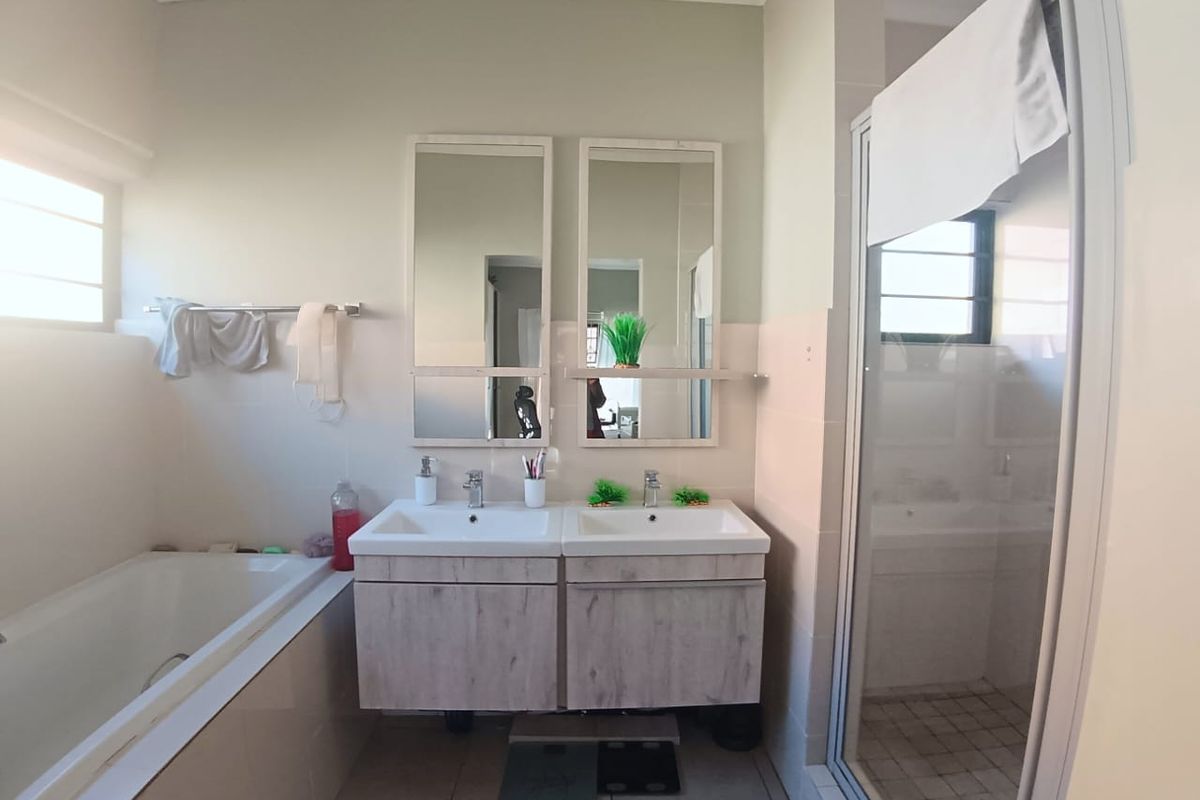 A functional bathroom featuring a double vanity with wood-look cabinetry, a built-in bathtub, and a separate glass-enclosed shower stall.