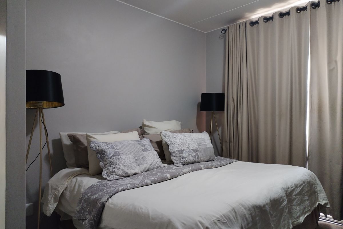 A well-maintained bedroom featuring neutral wall tones, floor-to-ceiling curtains, and ample natural light.