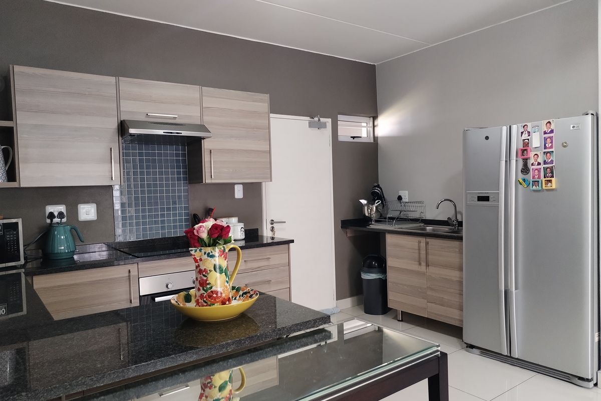 Modern kitchen featuring wood-grain cabinetry, dark granite countertops, tiled backsplash, built-in oven, extractor fan, and a double sink area.