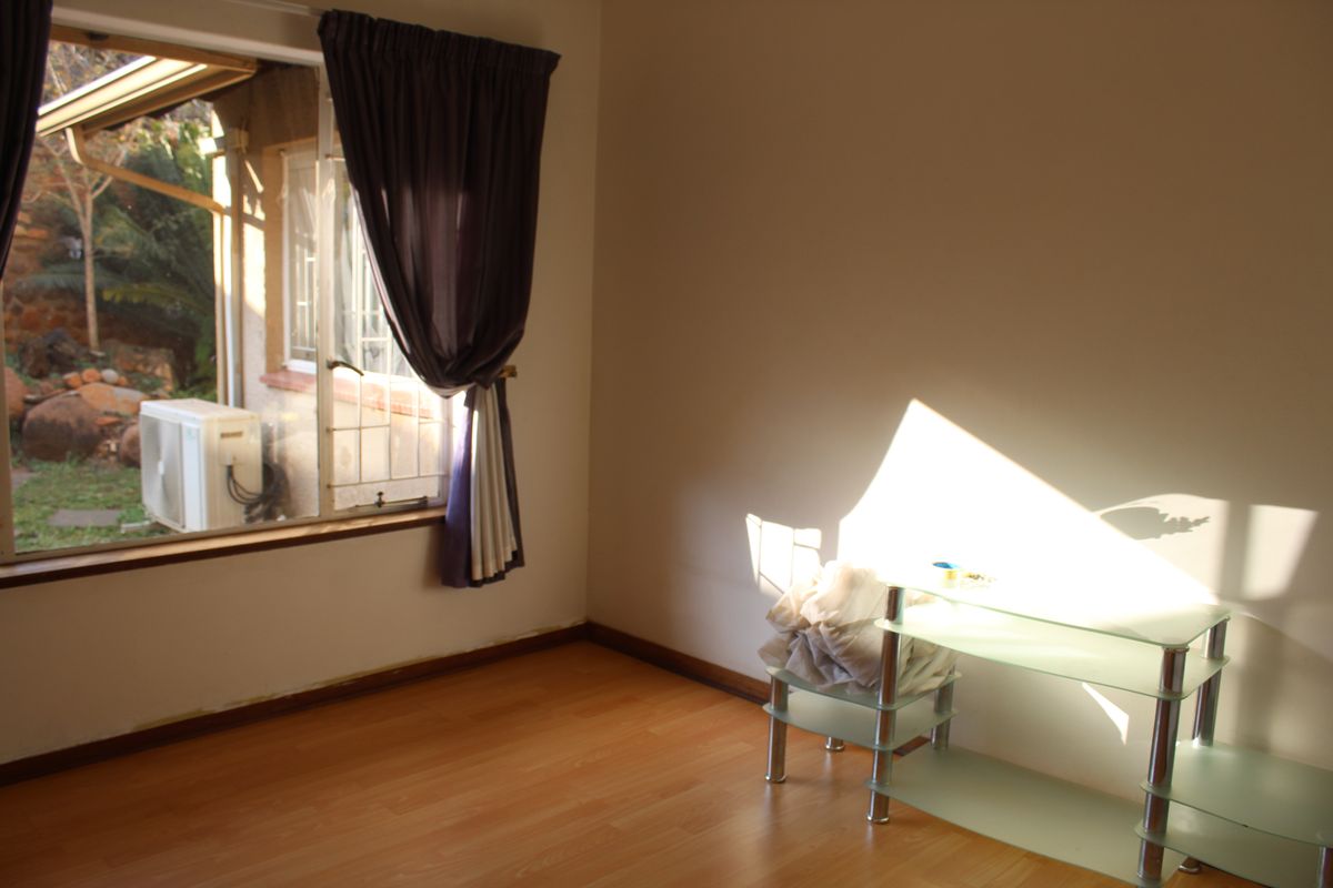 A sunlit bedroom featuring laminate wood flooring, a large window with garden views, and neutral wall finishes.