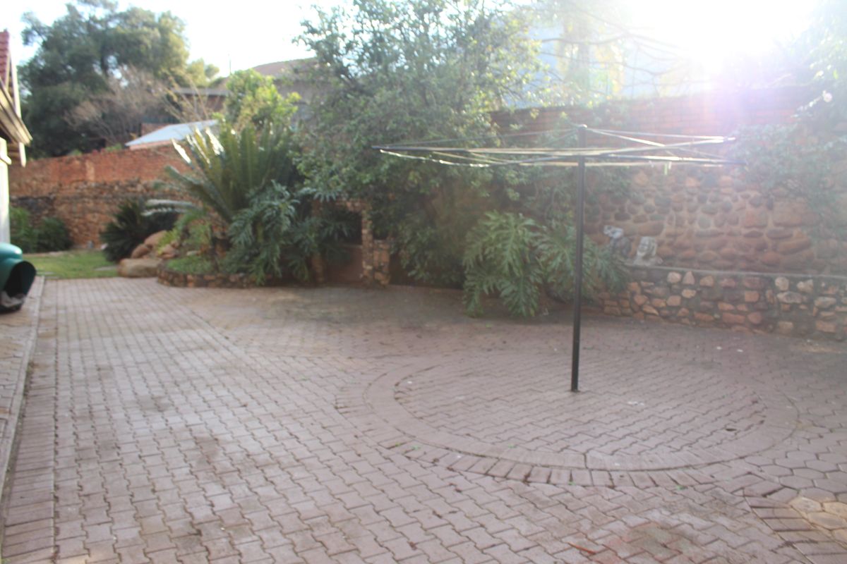 A paved rear courtyard area featuring a stone retaining wall, established garden beds, and a fixed rotary clothesline.