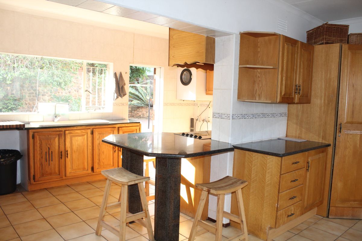 A functional kitchen featuring wooden cabinetry, dark granite countertops, a breakfast bar, and tiled flooring with direct access to the rear exterior.