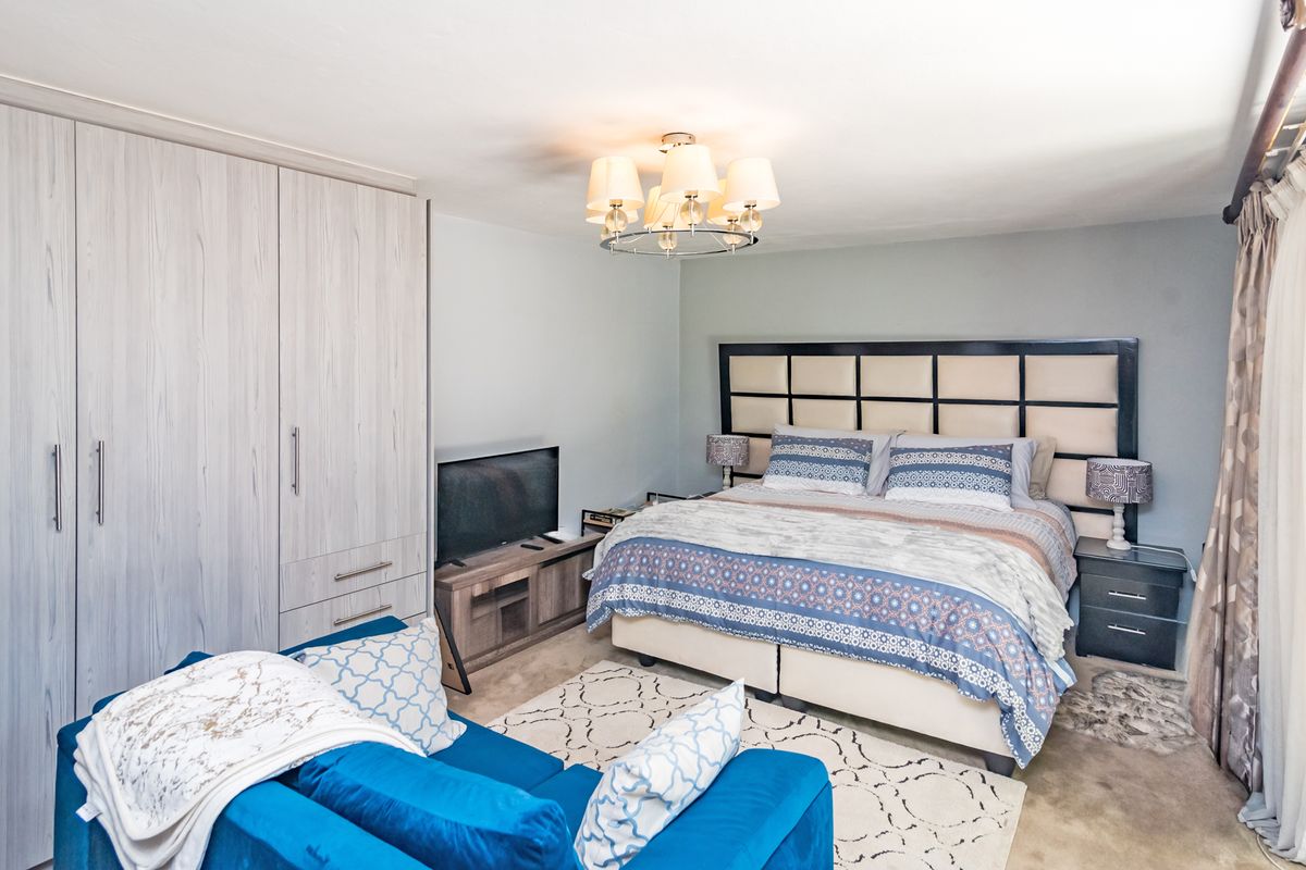A well-maintained bedroom featuring built-in wardrobes, a central chandelier, and neutral wall finishes, providing a comfortable and functional living space.