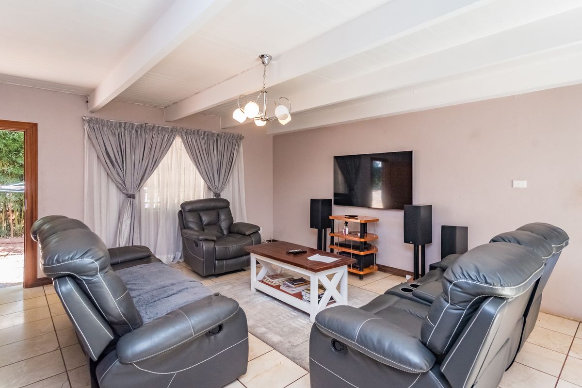 A comfortable living room featuring tiled flooring, exposed beam ceiling, and a wall-mounted television setup with direct access to the outdoor area.