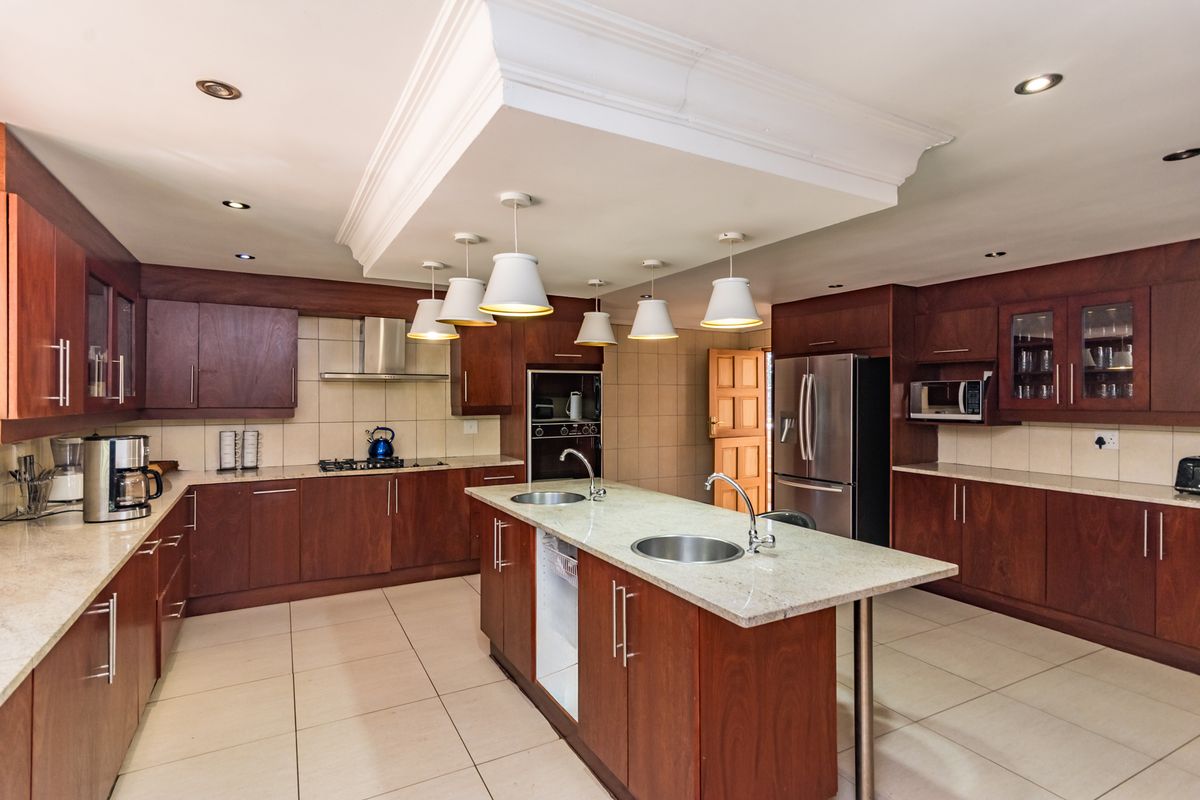 Spacious kitchen featuring dark wood cabinetry, granite countertops, a central island with dual sinks, and integrated stainless steel appliances.