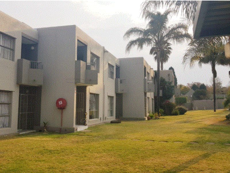 Rear view of a townhouse complex featuring multi-level units with balconies and a shared communal garden area.