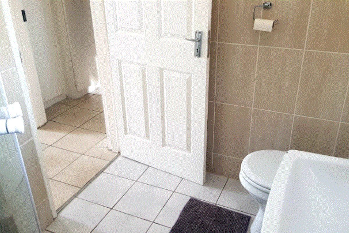 A functional bathroom featuring ceramic wall and floor tiling, a standard toilet, washbasin, and a glass-enclosed shower area.