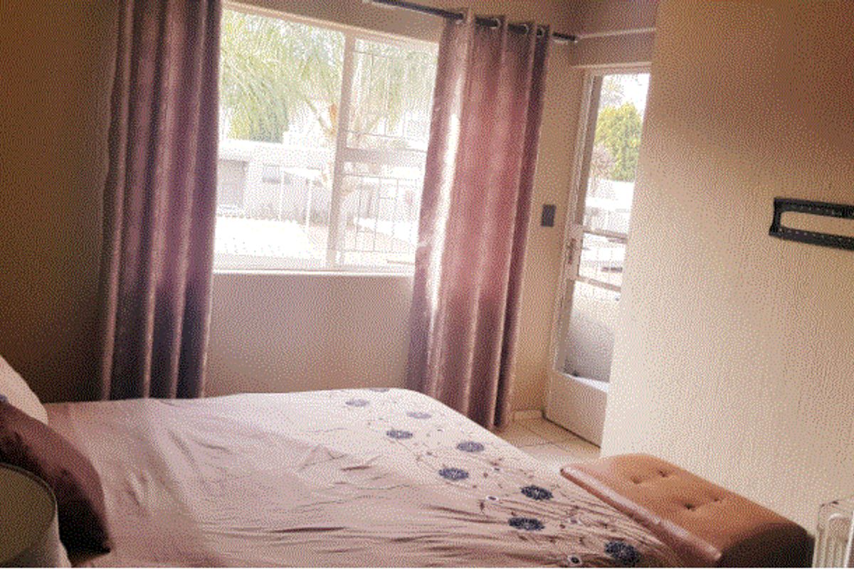 A bedroom featuring a window with natural light, a glass door leading outside, and a wall-mounted television bracket.