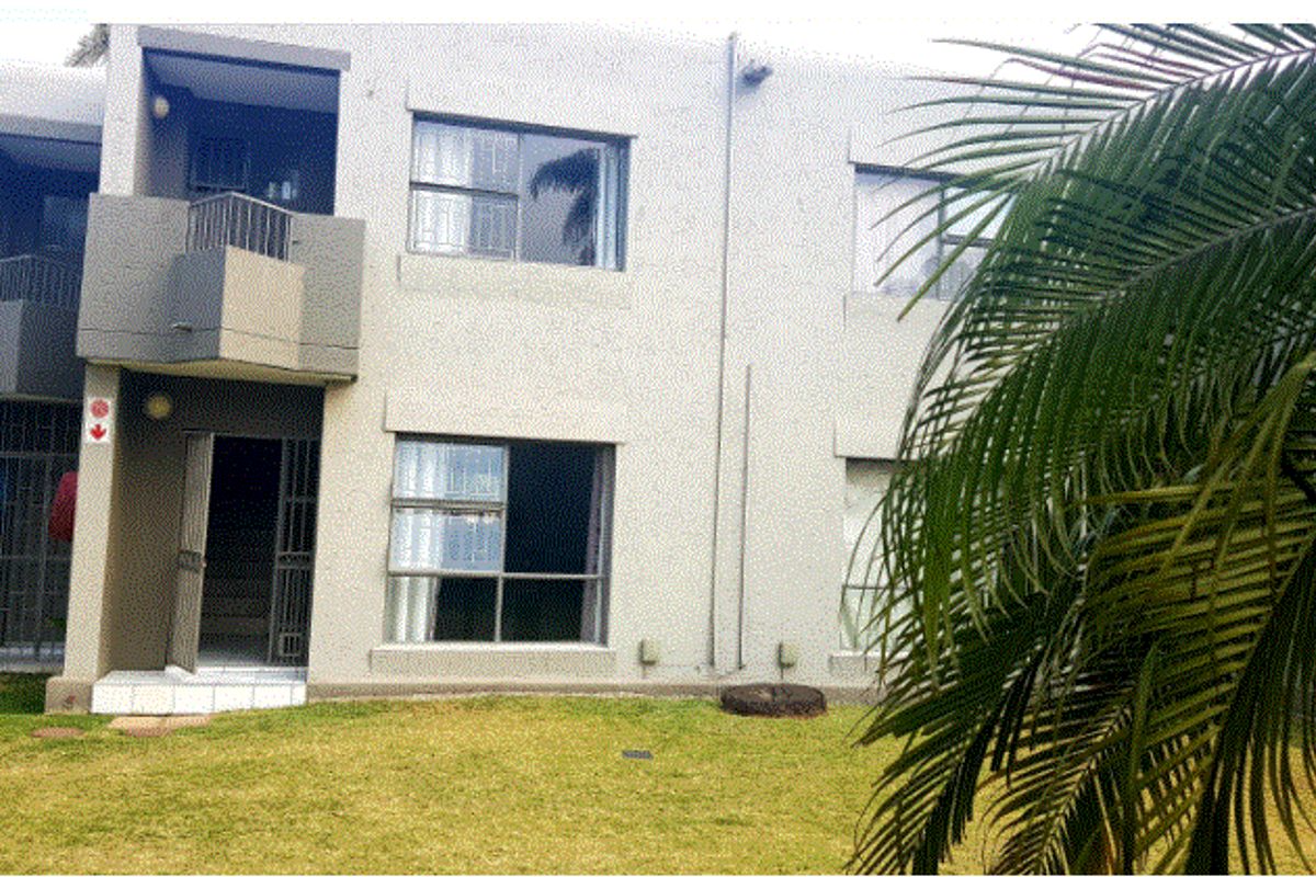Rear view of the townhouse featuring a small balcony, security gates, and sliding windows overlooking a shared garden area.