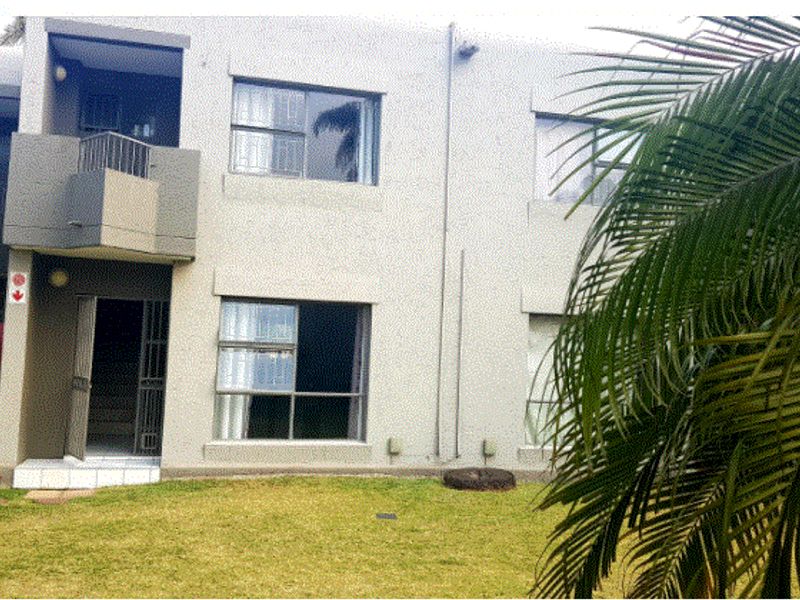 Rear view of the townhouse featuring a small balcony, security gates, and sliding windows overlooking a shared garden area.