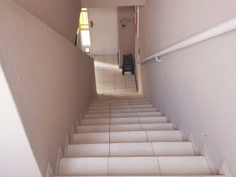 A functional tiled staircase featuring a wall-mounted handrail, leading down to an entry area with tiled flooring.