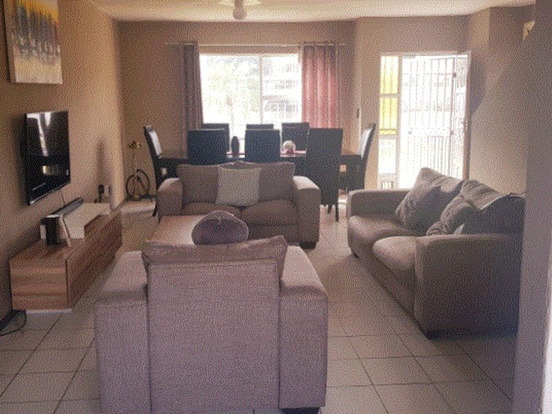 Open-plan living and dining area featuring tiled flooring, a ceiling fan, and access to an outdoor area through a security gate.
