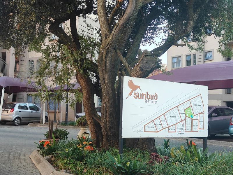 Entrance view of Sunbird Estate featuring a site map signage, mature trees, landscaped garden beds, and covered parking bays.