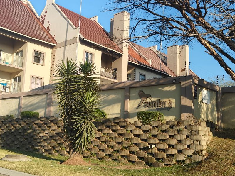 Front exterior view of Sunbird Estate apartment complex featuring a retaining wall, perimeter security fencing, and multi-story residential units with tiled roofing.
