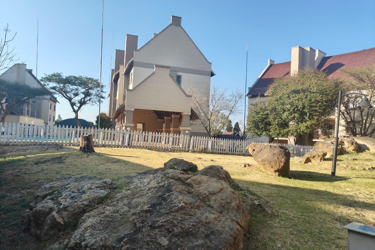 A view of the apartment complex exterior featuring a landscaped garden, large rock features, and a white picket fence surrounding the building.