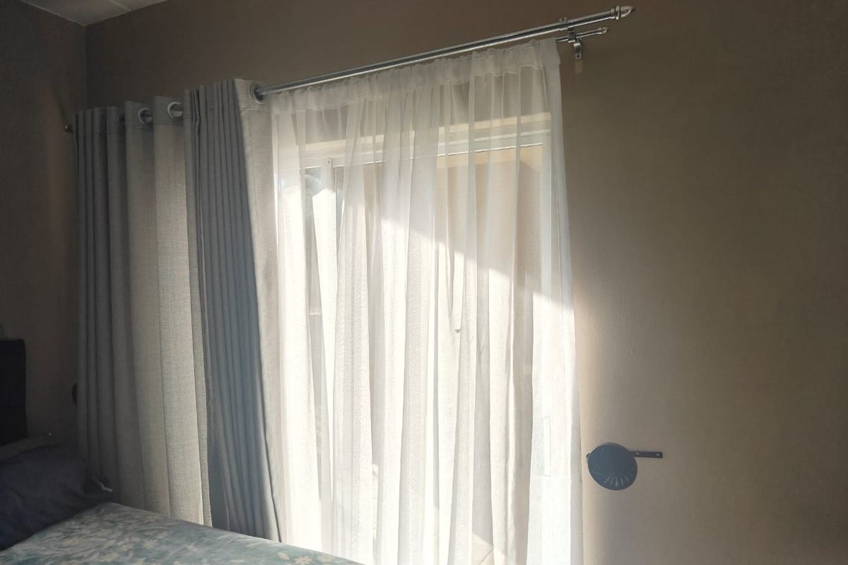 A bedroom interior featuring a sliding door with a double curtain rod system, allowing for natural light entry.