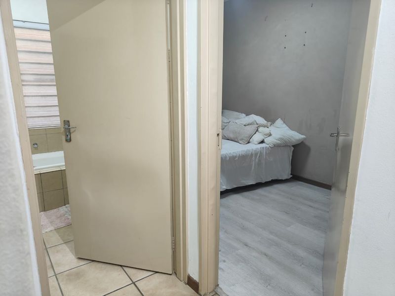 A hallway view showing access to a bedroom and a bathroom, featuring a mix of tiled and laminate flooring.
