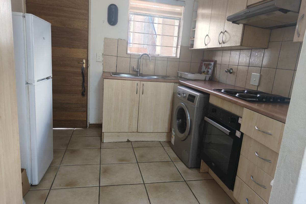 A functional kitchen featuring light wood-finish cabinetry, tiled backsplash, built-in oven and hob, and tiled flooring, offering a practical layout for daily use.