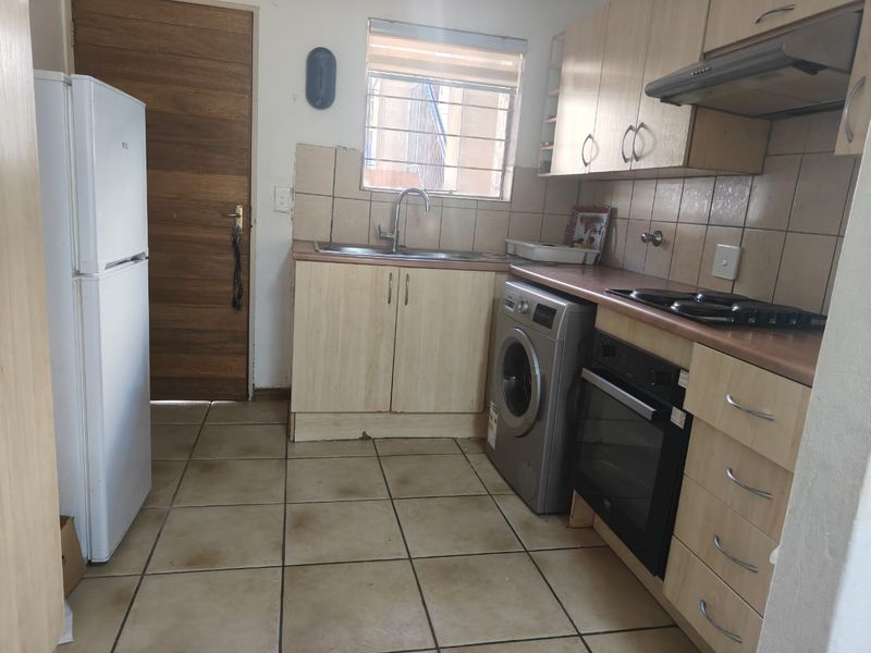 A functional kitchen featuring light wood-finish cabinetry, tiled backsplash, built-in oven and hob, and tiled flooring, offering a practical layout for daily use.