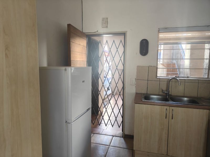 A compact kitchen area featuring laminate cabinetry, a double sink, and direct access to an exterior entrance protected by a security gate.