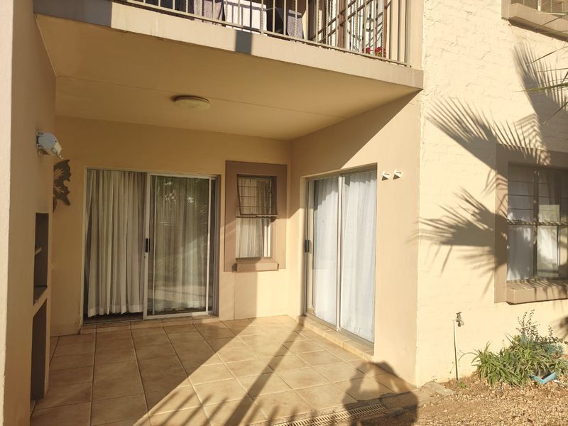 A covered ground-floor patio featuring tiled flooring, a built-in braai, and direct access to the interior through sliding glass doors.