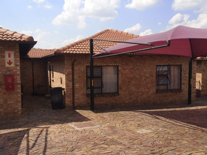 Front exterior view of a face brick townhouse featuring a paved driveway and a covered shade cloth carport.