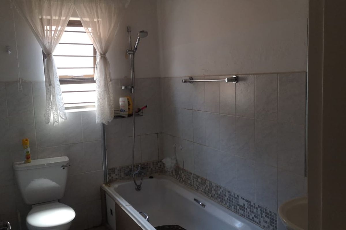 A functional bathroom featuring a bathtub with shower attachment, toilet, and tiled wall finishes, requiring some cosmetic updates to improve its overall condition.