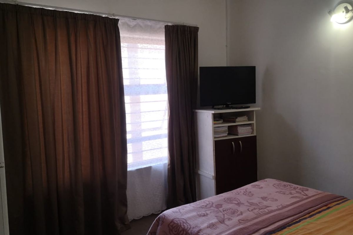 A standard bedroom featuring a window with curtains and a wall-mounted light fixture.