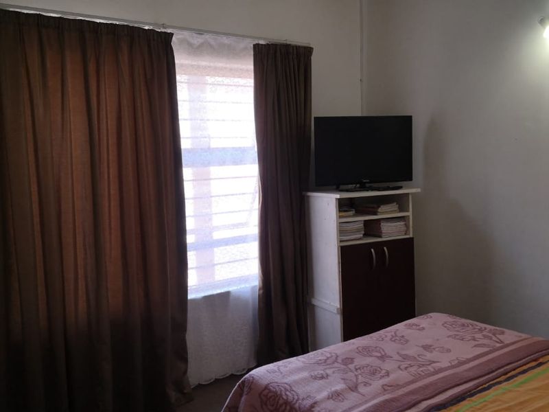 A standard bedroom featuring a window with curtains and a wall-mounted light fixture.