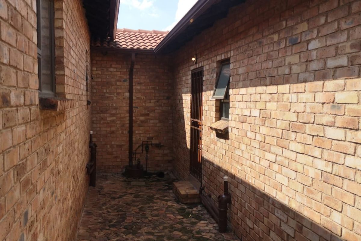 A side courtyard area featuring face brick walls, paved flooring, and a secure entrance gate, typical of a townhouse exterior utility space.